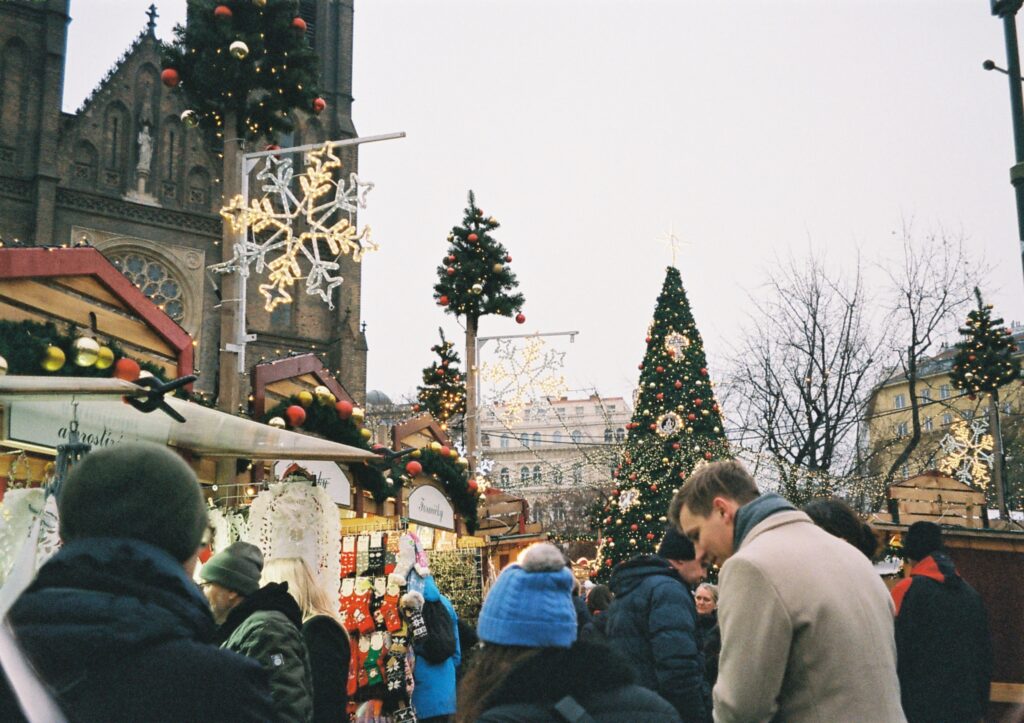 In questa foto è rappresentato un mercatino di natale; si possono notare alberi addobbati, una chiesa gotica e i piccoli negozietti.